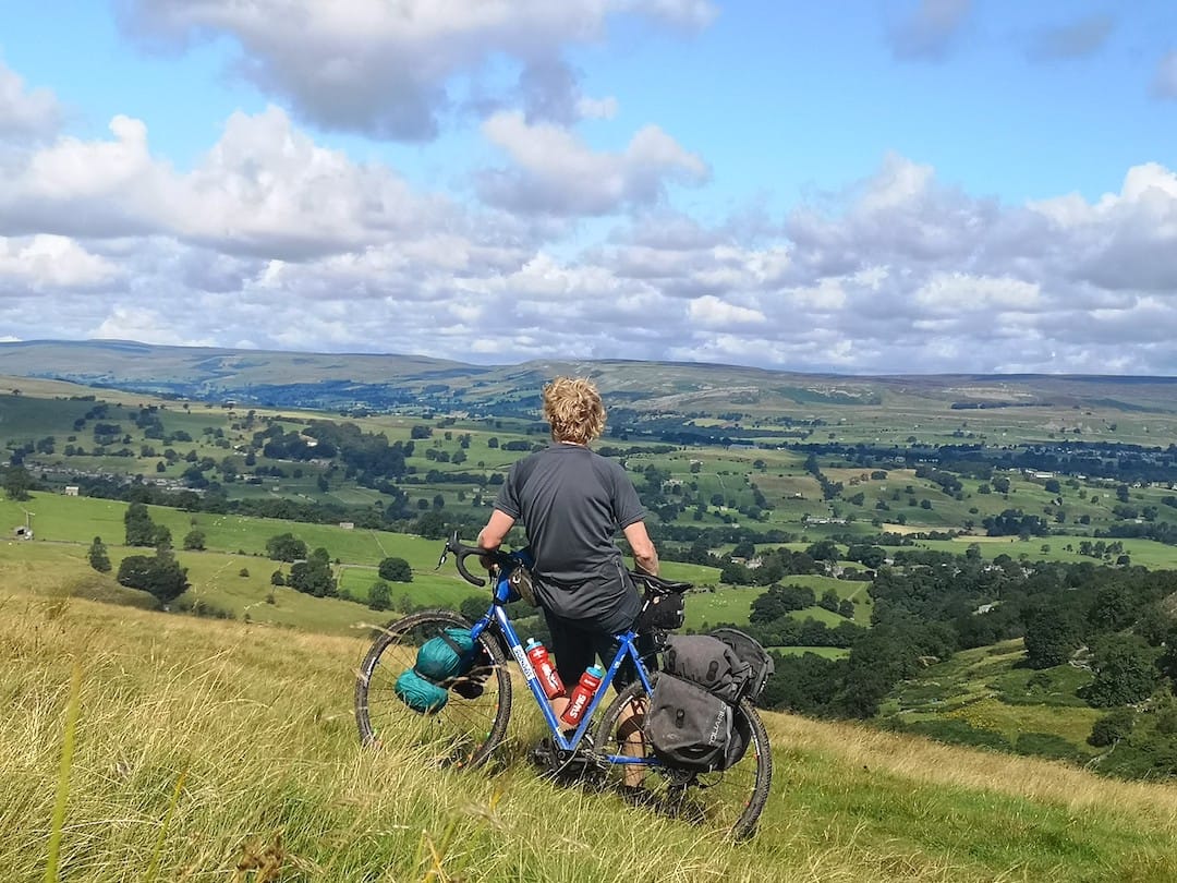 Picture shows Alastair with his bicycle looking out on to a green and hilly landscape