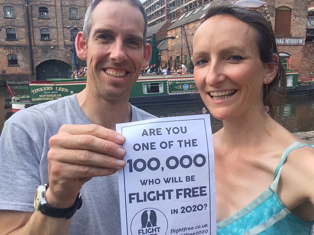 Anna Hughes and Etienne are taking a selfie together in front of a inner city canal. Etienne is holding a piece of paper with the Flight Free 2020 pedge on it. 